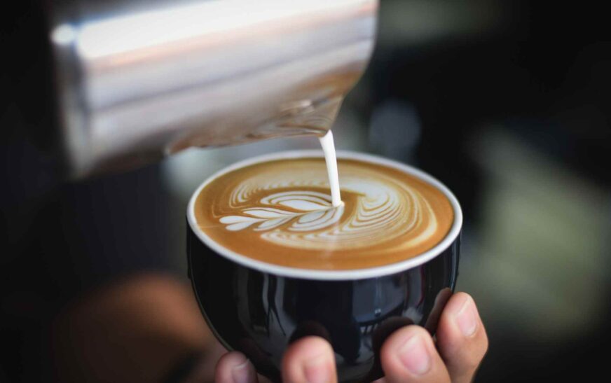 A barista adjusting the dial of an espresso grinder with coffee beans and scales in the background.